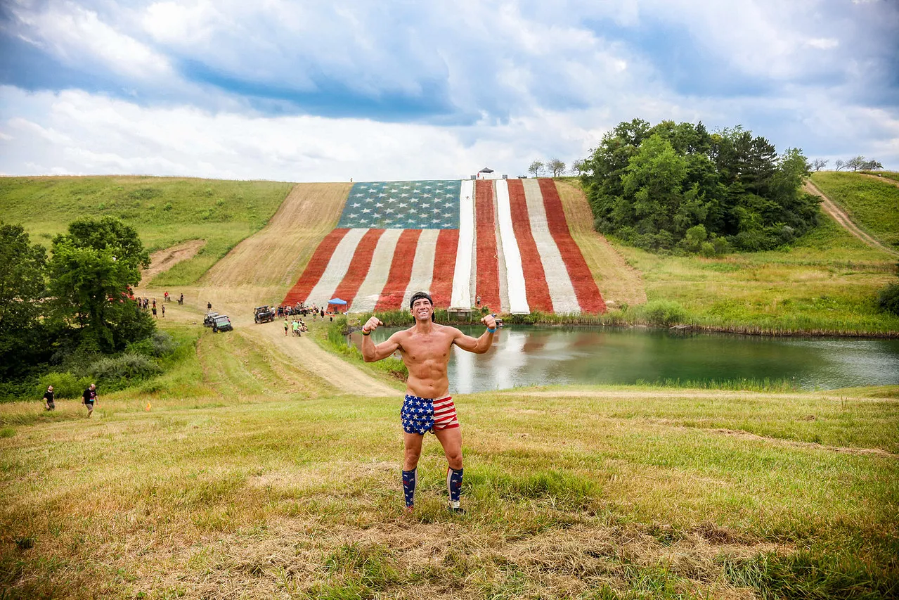 Smiling man with an American flag headband swimming in water with green algae.
